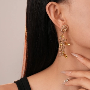 Close-up of gold dangle earrings featuring 'Beautiful' character and amber rhinestones