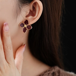 Detail of vintage burgundy enamel flower earring with gold trim on model ear