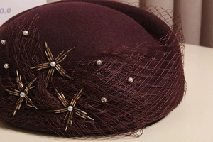 Detail of burgundy wool beret featuring elegant mesh veil with pearls and star beadwork
