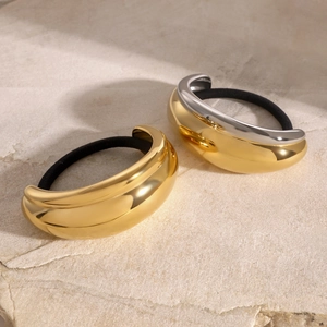Detail of high-polish gold and silver bicolor U-shaped metal hair ties on beige stone