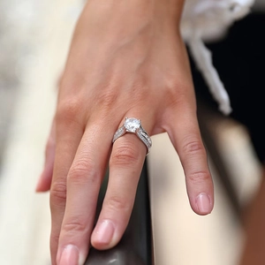 Macro view of four-prong set round diamond ring on finger with paved side stones