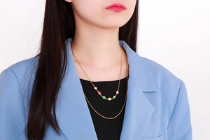 Detail shot of a double-layered gold necklace with colorful evil eye charms on a model