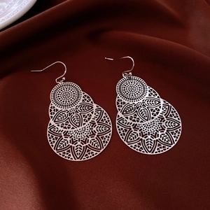Detailed view of silver hollow leaf floral earrings on dark premium silk fabric