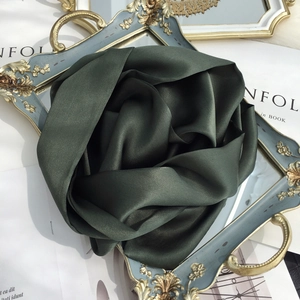 Detail of dark green mulberry silk scarf folded into a rose on a vintage tray