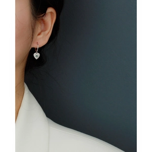 Macro view of silver heart-shaped dangle earrings featuring a green evil eye charm on model