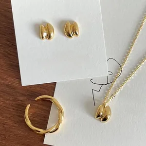 Flat lay of minimalist gold plated jewelry set with wrinkled pendant necklace and studs