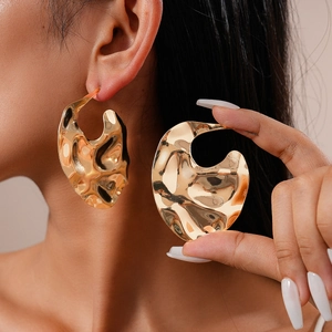 Détail de grandes boucles d'oreilles dorées à texture métal liquide irrégulière sur modèle
