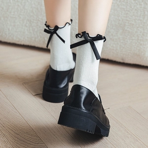 Detail of white cotton calf socks featuring ruffled edges and black satin bows