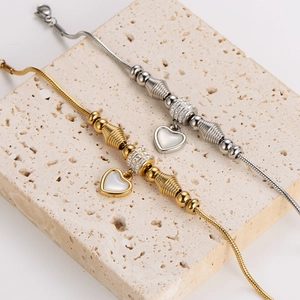 Elegant gold and silver snake chain bracelets with heart pendants on a beige stone stand