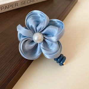 Détail d'un chouchou fleur en tissu bleu avec perle et élastique en cordon spirale
