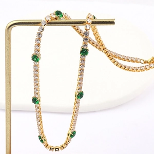 Macro detail of gold tennis necklace featuring sparkling zircons and green emerald stones