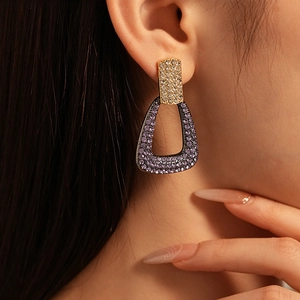 Macro shot of a model wearing geometric purple and gold rhinestone-set earrings
