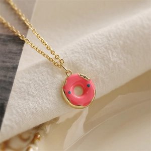 Macro view of golden necklace featuring a pink enamel donut pendant with blue sprinkles