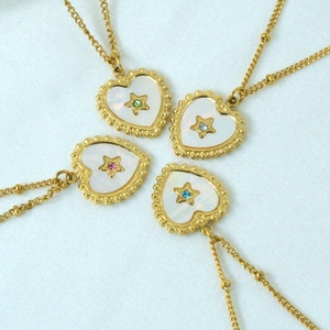 Four 14K gold plated heart shell necklaces with colorful star crystals on white fabric