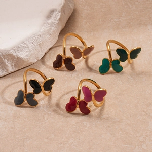 Elegant gold butterfly rings with colorful enamel wings on minimalist stone surface