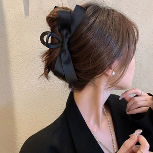 Detail of elegant black satin bow hair claw clip worn on model for sophisticated styling