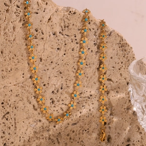 Detail of 18K gold-plated chain with blue floral charms on natural stone background