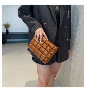 Gros plan sur la pochette en cuir PU matelassé marron caramel tenue par un mannequin
