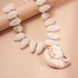 Detailed macro view of white acrylic beads and golden spacers with a nautilus shell pendant