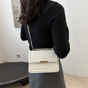 White chevron quilted crossbody bag with gold chain strap shown on a model's shoulder