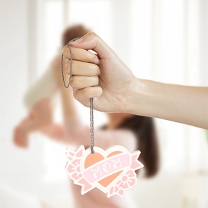 Dettaglio del ciondolo a cuore per la Festa della Mamma con scritta MOM e decoro floreale