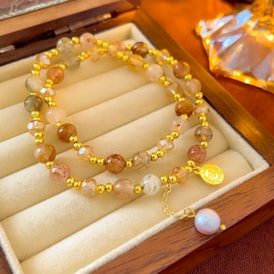 Detail of double-layer beaded bracelet with natural stone, gold charm, and white pearl