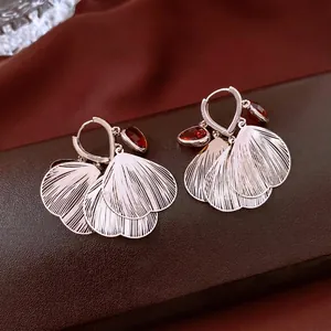 Elegant silver hollow leaf earrings with red ruby zircon stones on a luxury background