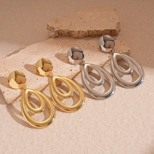 Polished hollow drop earrings in gold and silver finish on textured stone surface