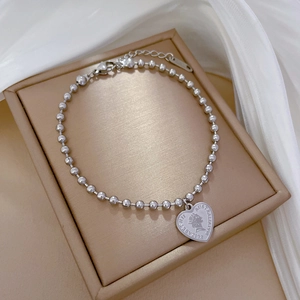 Detailed macro view of heart charm bracelet with royal portrait engraving and bead chain
