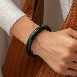 Close-up of a vintage dark green marble acrylic bangle on wrist with woven bag background