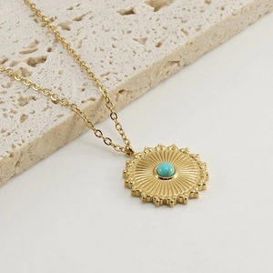 Gold stainless steel sunburst necklace with turquoise stone on beige stone slab