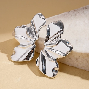 Macro shot of silver-colored irregular petal earrings on white stone texture