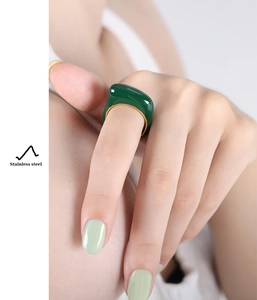 Close-up of gold-plated stainless steel ring with emerald green resin inlay on finger