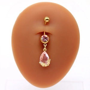 Dettaglio di un piercing all'ombelico dorato con zircone rosa a goccia e filigrana