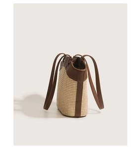 Close-up of beige straw texture and brown leather trim on the bucket shoulder bag