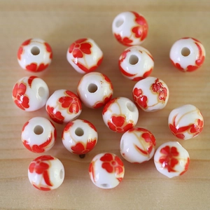 Close-up of ceramic beads with red flower patterns and holes for DIY jewelry