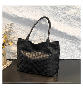 Close-up of black woven leather tote bag texture on elegant wooden surface