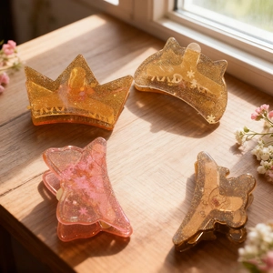 Set of four resin hair clips in crown, bear and bow shapes with sparkling gold glitter