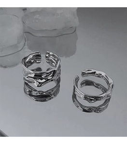 Detailed close-up of irregular silver lava texture open rings on a metallic surface