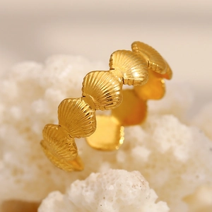 Vue macro de bagues coquillage en or sur corail blanc au design océanique épuré