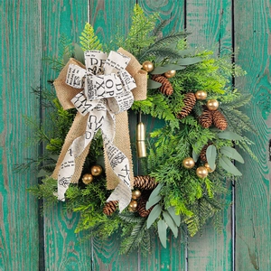 Rustic Christmas wreath with pine cones, golden bells, and vintage letter print bow.