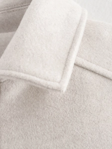 Detailaufnahme des Kragens und der Textur einer cremefarbenen Tweedjacke mit feinen Nähten