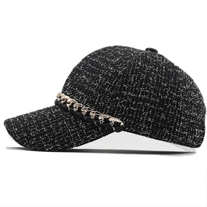 Close-up of black tweed baseball cap featuring a decorative gold chain and textured fabric