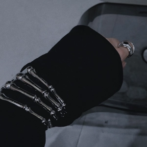 Close-up of polished silver skeleton hand bracelet and ring with dark gothic aesthetic