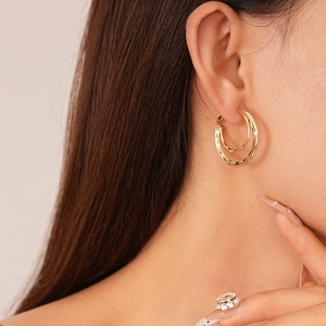Detail view of layered geometric golden metal double hoop earrings worn by a model