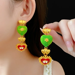 Close-up of vintage gold earrings with green and red enamel heart and pearl details