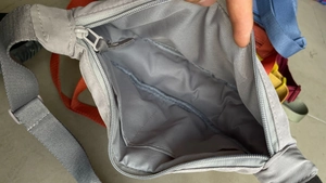 Detail showing the inner compartment and zipper closure of the grey nylon crossbody bag