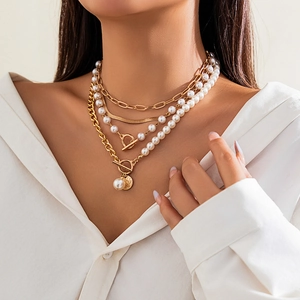 Detail of layered gold chain necklace featuring baroque pearls and a stylish T-bar toggle