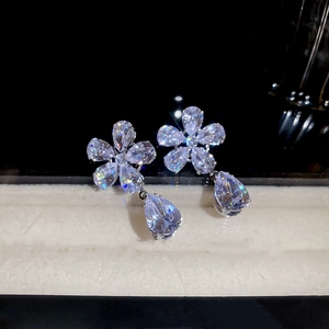 Macro shot of silver flower earrings with teardrop zircon pendants on dark reflective surface