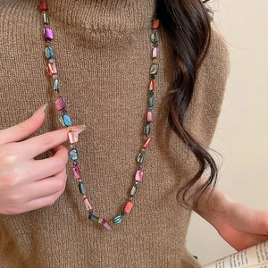 Detail of a colorful shell beaded long necklace styled on a brown knit sweater
